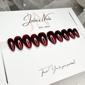 May include: A set of ten red ombre press-on nails with a white accent on each nail. The nails are displayed on a white card with the text "Julie's Nails Est. 2024" and "Thank You for your purchase!"