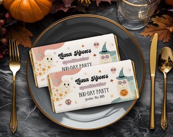 May include: Two Halloween chocolate bars on a grey plate with gold cutlery. The bars feature a ghost and a witch with the text "Luna Moons spooktacular BOO-DAY PARTY October 31st 2025". Pumpkins and autumn leaves surround the plate.
