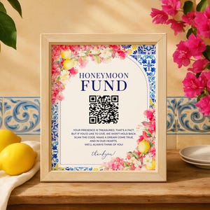 May include: A framed sign with the words "HONEYMOON FUND" and a QR code. The sign is decorated with floral and lemon accents. The text below the QR code reads, "Your presence is treasured..." Two lemons and a sprig of lemons are in the image.