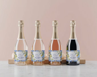 May include: Four miniature champagne bottles with personalised labels. The labels feature a blue and white tiled pattern with lemons and greenery. The text on the labels reads "Cheers!" and "Mrs. Smith".