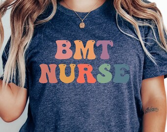 May include: A navy blue t-shirt with the text "BMT NURSE" in rainbow colors. The letters are stylized with rounded edges.