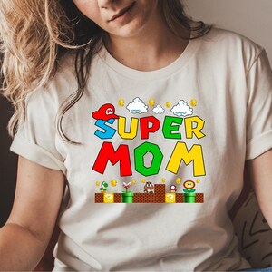 May include: White t-shirt with a colorful graphic of a video game character and the text "SUPER MOM".
