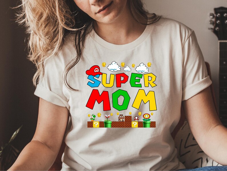 May include: White t-shirt with a colorful graphic of a video game character and the text "SUPER MOM".