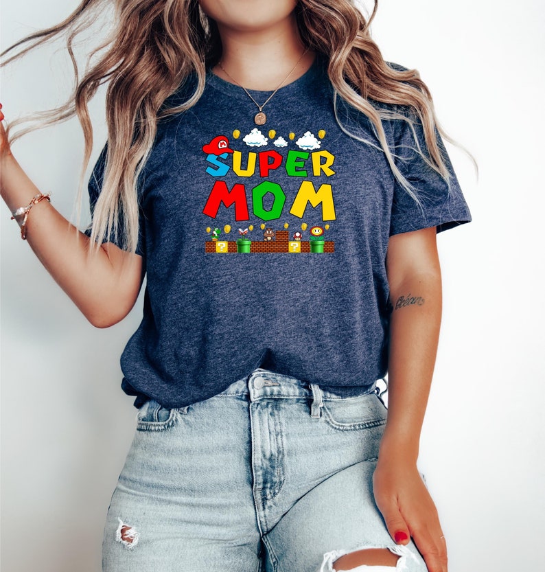 May include: A navy blue t-shirt with a graphic of a Super Mario-themed design that says "SUPER MOM" in colorful letters. The graphic also includes a mushroom, a question mark block, and a star.