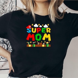 May include: Black t-shirt with a graphic of a Super Mario-themed design that says "SUPER MOM" in colorful letters.