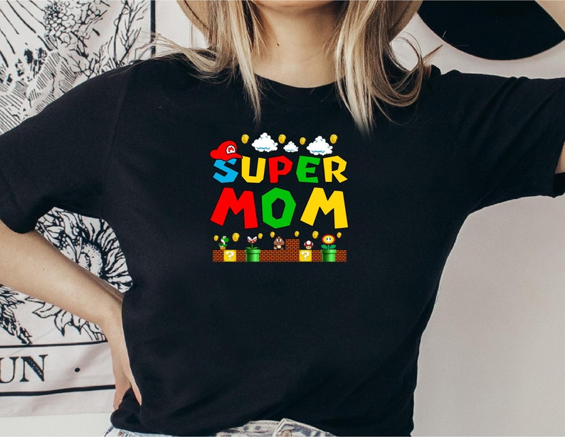 May include: Black t-shirt with a graphic of a Super Mario-themed design that says "SUPER MOM" in colorful letters.