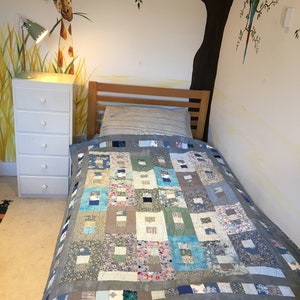 May include: A single bed with a blue and grey patchwork quilt. The bed is in a room with a white wall and a mural of a giraffe and a tree with a parrot.