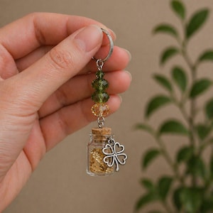 May include: A keyring with a small glass bottle filled with gold flakes, a cork stopper, and a silver shamrock charm. Green and yellow beads are also attached. The background is a neutral colour.