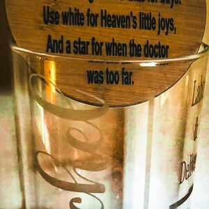 May include: A clear glass container filled with colorful beads, topped with a wooden disc inscribed with a poem. The beads are pink, blue, green, and clear. The glass has cursive text on it.