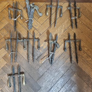 May include: A collection of antique door handles with ornate designs. The handles are made of metal and have a brass finish. They are arranged in rows on a wooden floor.