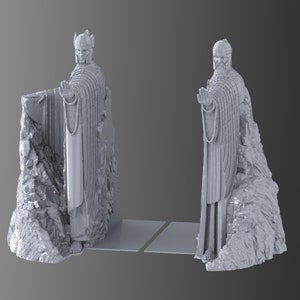 May include: A pair of bookends featuring a gray, sculpted figure of a man in a robe standing on a rocky base. The figures are facing opposite directions and have their hands raised.