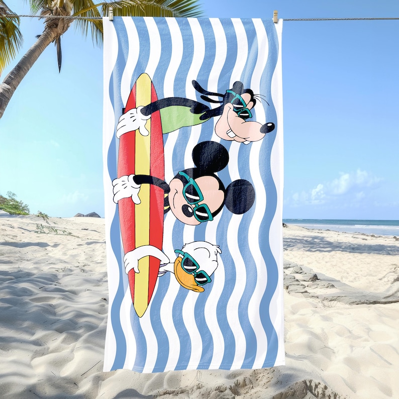 May include: A white beach towel with blue and white stripes. Mickey Mouse, Goofy, and Donald Duck are on the towel, riding a surfboard. They are all wearing sunglasses.