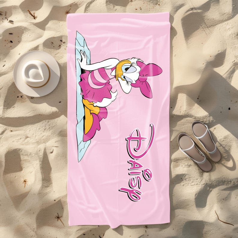 K&ouml;nnte beinhalten: Rosa Strandtuch mit einem Cartoon-Bild von Daisy Duck, die ein rosa Kleid und eine Schleife tr&auml;gt. Das Handtuch tr&auml;gt den Text "Disney Daisy" in rosa Schrift.