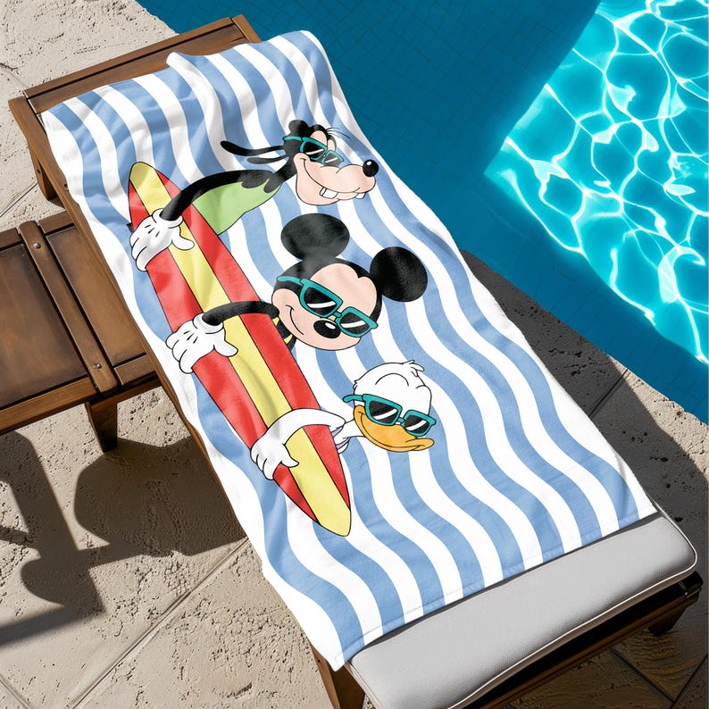 May include: A white beach towel with blue and white stripes and a wave pattern. Mickey Mouse, Goofy, and Donald Duck are on the towel, riding a surfboard and wearing sunglasses.