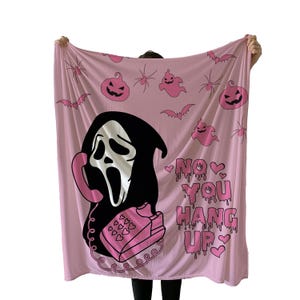 May include: Pink blanket featuring a black and white Ghostface character holding a pink telephone. The blanket has pink pumpkins, ghosts, spiders, and bats. Text on the blanket reads "NO YOU HANG UP" in pink.