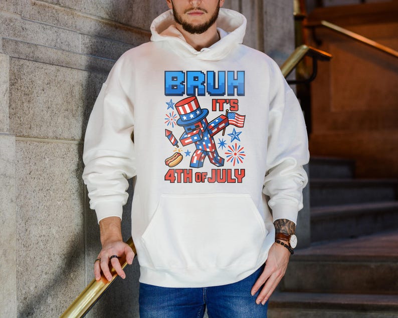 Puede incluir: Sudadera con capucha blanca con un gr&aacute;fico que dice "BRUH IT'S 4TH OF JULY". El gr&aacute;fico presenta un personaje patri&oacute;tico con un sombrero de copa, sosteniendo una bandera y un perrito caliente, con fuegos artificiales y estrellas.