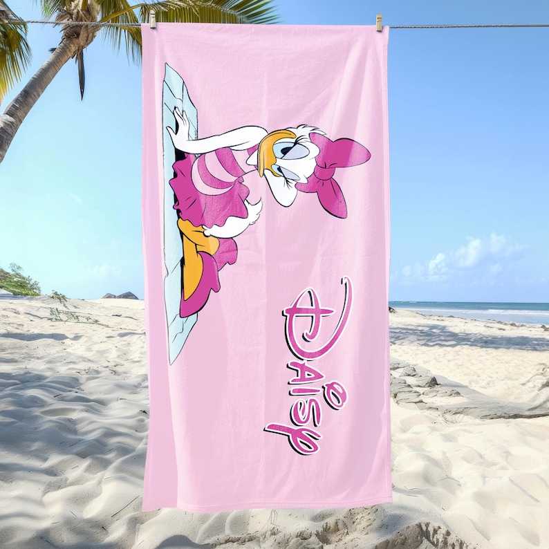 K&ouml;nnte beinhalten: Rosa Strandtuch mit einem Cartoon-Bild von Daisy Duck in einem rosa Kleid mit einer gelben Schleife. Das Handtuch tr&auml;gt den Text "Disney Daisy" in rosa Schrift.