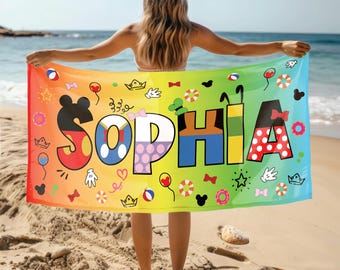 Op de afbeelding: Een kleurrijke strandhanddoek met de naam "Sophia" in grote letters. Elke letter is versierd met verschillende Disney-figuren en iconen, waaronder Mickey Mouse, Minnie Mouse, Donald Duck en Goofy. De handdoek is een regenboog van kleuren, met een gele achtergrond en rode, oranje, groene, blauwe en paarse accenten.