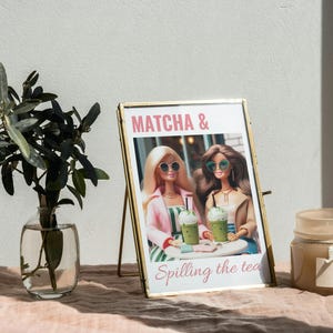 Puede incluir: Imagen enmarcada en oro con dos mu&ntilde;ecas sosteniendo bebidas verdes. La imagen dice "MATCHA & Spilling the tea".