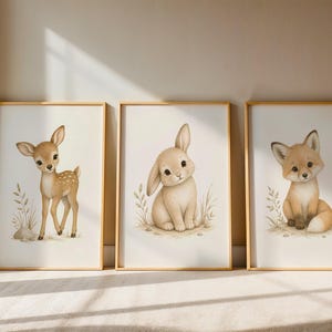 May include: Three framed wall art prints featuring illustrations of woodland animals. The left print shows a fawn, the centre print shows a rabbit, and the right print shows a fox. Each animal is depicted in a soft, neutral colour palette.