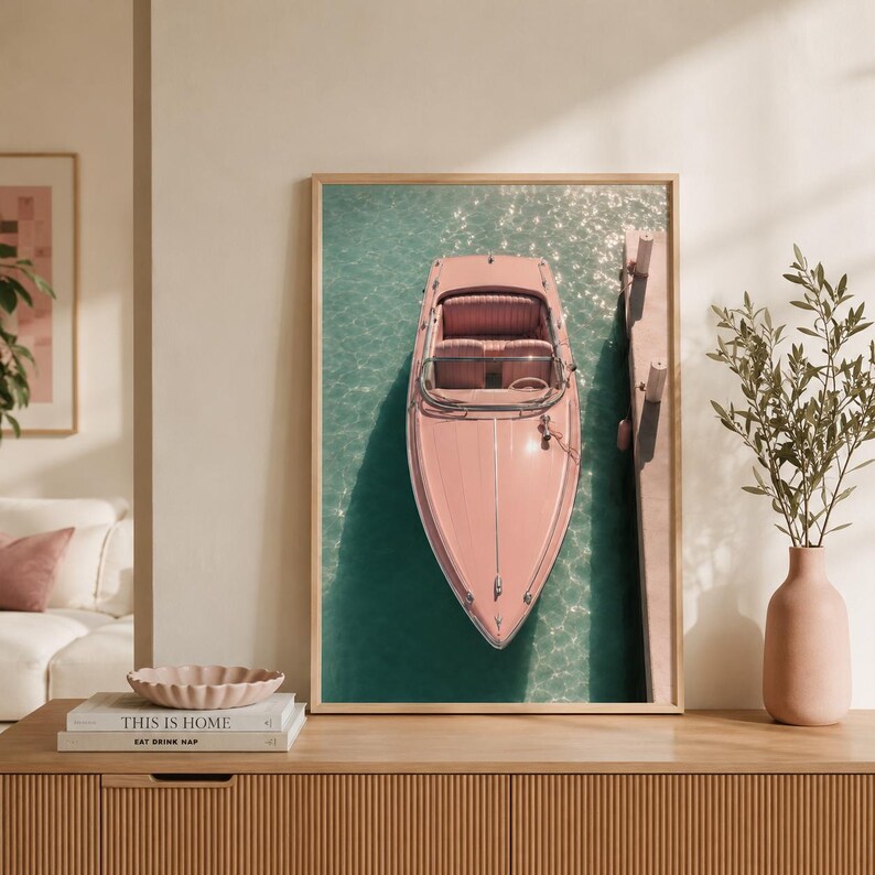 May include: A framed vertical wall art print featuring a top-down view of a pastel pink motorboat docked alongside a wooden pier in clear turquoise water. The boat has a windshield and bench seating, captured in a bright, sunlit outdoor setting.