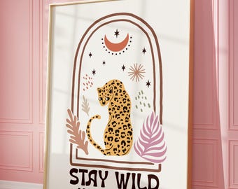 May include: A framed art print featuring a stylized leopard with a spotted coat, set within an arched frame. The artwork includes a crescent moon, stars, and the text "STAY WILD * MOON CHILD *" in a bold font. The color palette includes beige, brown, and pink.