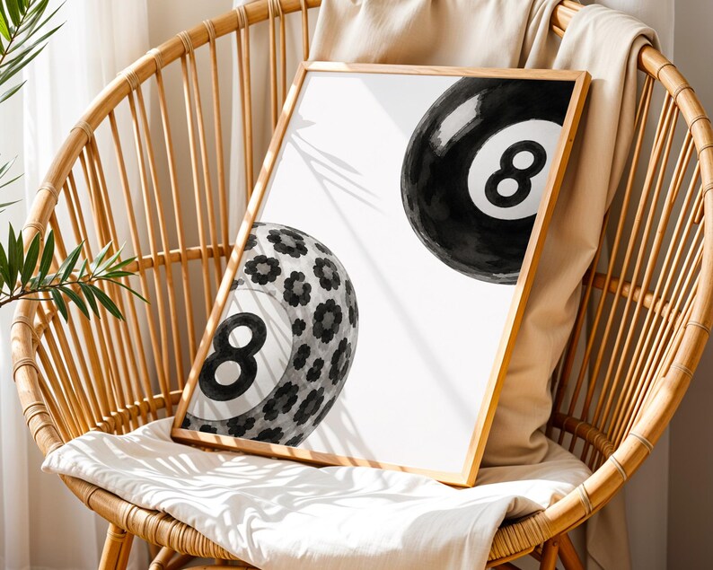 May include: A rectangular framed print featuring two black and white eight balls on a white background. One ball is solid black with a white number eight, while the other ball is patterned with black and gray floral shapes and a white number eight.