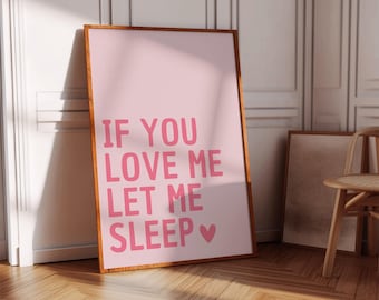 May include: A framed pink print with the text "IF YOU LOVE ME LET ME SLEEP" in pink letters. The print is in a wooden frame and leans against a white wall. A wooden chair and another framed print are in the background.