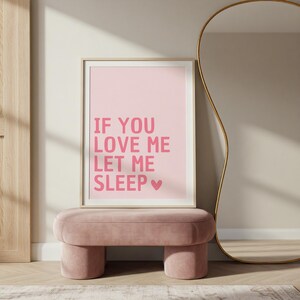 May include: A framed pink print with the text "IF YOU LOVE ME LET ME SLEEP" in pink letters, with a pink heart symbol. The print is displayed above a pink velvet ottoman with rounded legs.