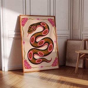 Könnte beinhalten: Ein gerahmter Kunstdruck mit einer stilisierten Schlangenillustration. Die Schlange ist in Grün-, Rosa- und Gelbtönen dargestellt, mit einer rosa Zunge. Das Kunstwerk ist in einem Holzrahmen gerahmt und hat dekorative florale Elemente.