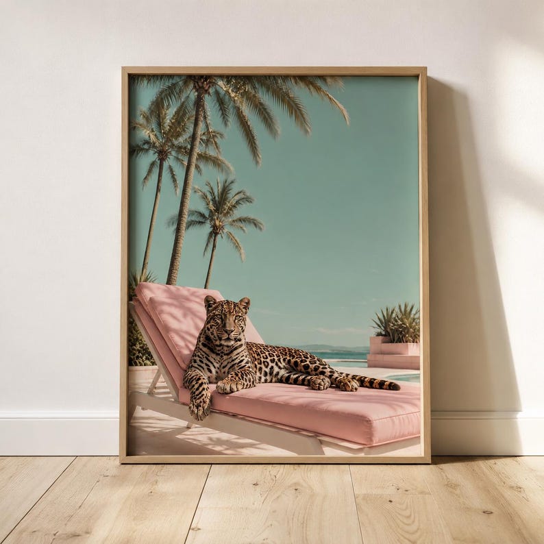 May include: A framed wall art print featuring a leopard resting on a pink lounge chair. The scene includes tall palm trees against a clear sky and a glimpse of a swimming pool. The artwork is encased in a light-colored wooden frame.