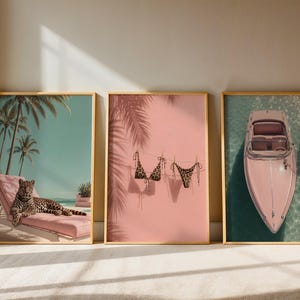 May include: Three framed wall art prints featuring a leopard resting on a pink lounge chair under palm trees, a leopard print bikini hanging on a clothesline against a pink wall with palm shadows, and a pink boat docked in turquoise water.