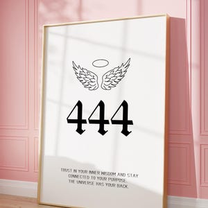 May include: A framed art print with a gold frame, featuring the number "444" in black gothic font, angel wings, and the text "TRUST IN YOUR INNER WISDOM AND STAY CONNECTED TO YOUR PURPOSE. THE UNIVERSE HAS YOUR BACK."