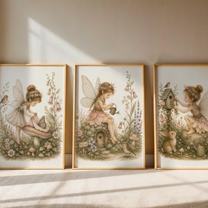 May include: Three framed wall art prints featuring illustrations of fairies in a garden setting. The first shows a fairy with a butterfly on a mushroom, the second a fairy watering flowers near a stone house, and the third a fairy with a birdhouse.