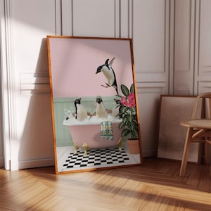 以下が含まれることがあります： ピンクのバスタブで泡と遊ぶペンギンの額入りアートプリント。1羽のペンギンが飛び込み、他のペンギンはリラックスしています。プリントは木製のフレーム、白黒の市松模様の床、鉢植えの植物があります。