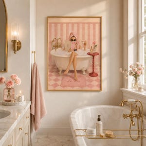 May include: A framed wall art print depicting a person in a clawfoot bathtub filled with bubbles, reading a magazine titled Vogue. The scene features pink striped walls, a checkered floor, and a small side table with a rose in a glass vase.