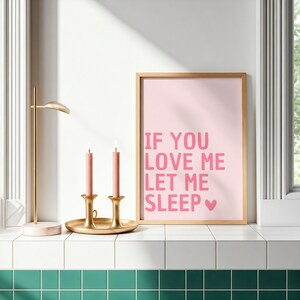 May include: A framed pink print with the text "IF YOU LOVE ME LET ME SLEEP" in pink. Two pink candles sit in gold candle holders on a gold tray. A gold desk lamp is to the left.