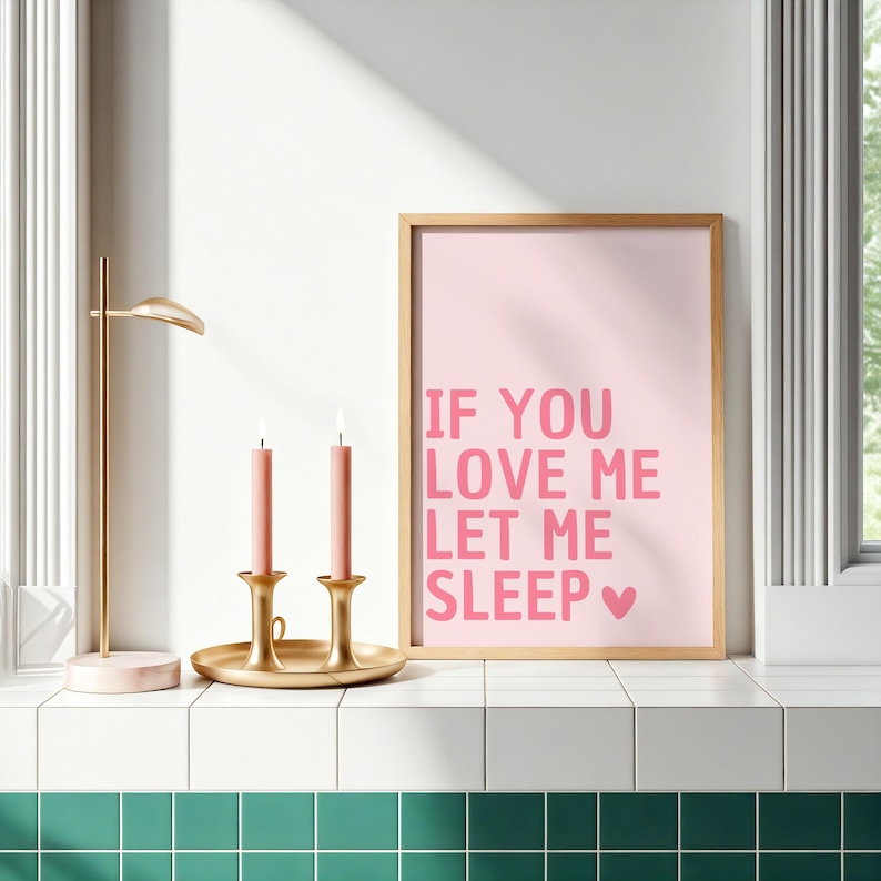 May include: A framed pink print with the text "IF YOU LOVE ME LET ME SLEEP" in pink. Two pink candles sit in gold candle holders on a gold tray. A gold desk lamp is to the left.