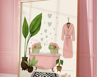 Puede incluir: Una impresión artística enmarcada con dos ranas de dibujos animados en una bañera rosa, con gorros de baño rosas. Una bata rosa cuelga cerca. La escena incluye plantas, una alfombra y zapatillas, todo sobre una pared rosa.