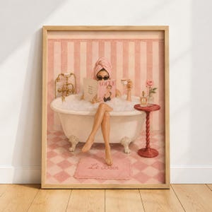 May include: A framed wall art print depicting a person in a clawfoot bathtub filled with bubbles, wearing a pink towel wrap and sunglasses while reading a Vogue magazine. A small side table holds a teacup and a rose in a glass vase.