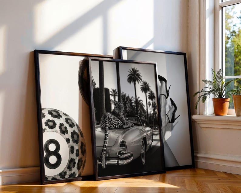 May include: Three framed black and white wall art prints. The left print shows a large number eight billiard ball with a floral pattern. The center print features a leopard resting on the back of a vintage convertible car with palm trees. The right print displays a pair of legs wearing high-heeled shoes.
