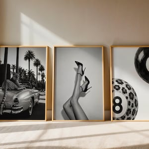 May include: Three framed black and white wall art prints. The left print shows a leopard on a vintage convertible car with palm trees. The center print displays legs in high-heeled shoes. The right print features two eight-ball billiard balls.