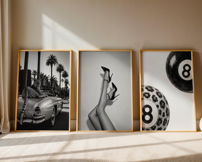 May include: Three framed black and white wall art prints. The left print shows a leopard on a vintage convertible car with palm trees. The center print displays legs in high-heeled shoes. The right print features two eight-ball billiard balls.