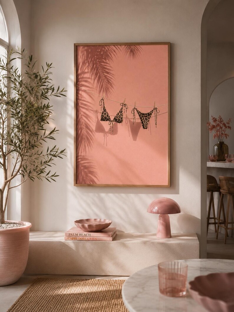 May include: A framed wall art print featuring a coral-colored background with a clothesline displaying a leopard print bikini top and bottom, accompanied by the shadows of palm fronds cast across the surface of the artwork.