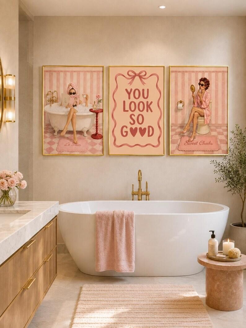 May include: A set of three framed wall art prints featuring pink and white striped backgrounds. The left print shows a person in a bathtub, the center print displays the text YOU LOOK SO GOOD with a bow, and the right print shows a person with a mirror.