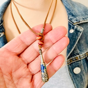 May include: A brown leather cord necklace with a silver and blue cone-shaped pendant. The pendant has intricate gold detailing and is accented with two brown wooden beads.