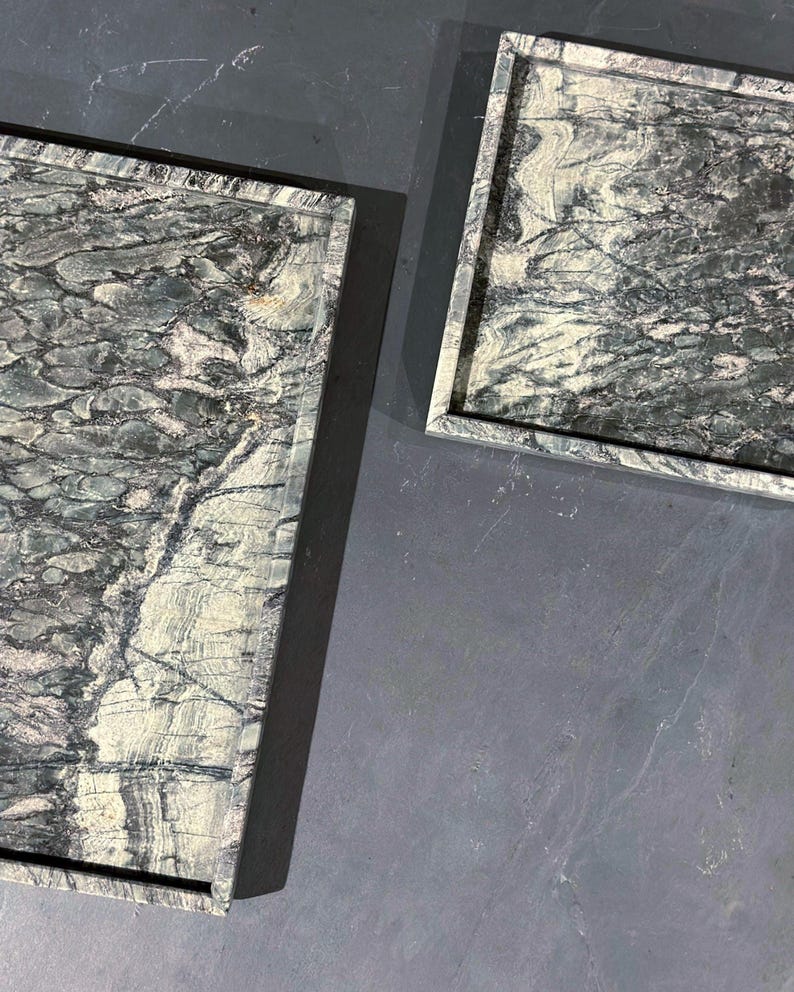 May include: Two rectangular trays with a dark gray and white marble pattern. The trays have a raised edge and are set against a gray background. The marble has a natural, flowing design.