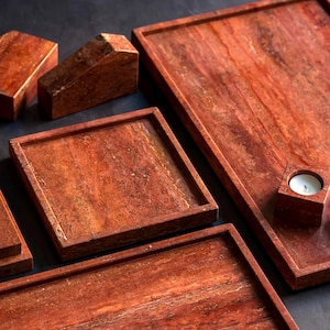 Könnte beinhalten: Eine Sammlung von rotbraunen Steintabletts und dekorativen Objekten. Das Set umfasst rechteckige und quadratische Tabletts, einen Kerzenhalter und geometrische Formen. Der Stein hat ein natürliches, geädertes Muster.