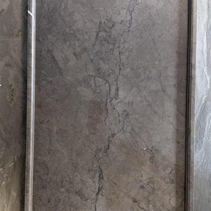K&ouml;nnte beinhalten: Ein rechteckiges Tablett aus grauem Marmor mit polierter Oberfl&auml;che. Die Fl&auml;che weist durchgehend nat&uuml;rliche, dunkelgraue Aderungen auf, und das Tablett ist von einem erh&ouml;hten, glatten Rand umgeben, der entlang aller vier Seiten verl&auml;uft.