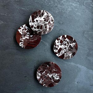 Könnte beinhalten: Vier runde Untersetzer aus rotem und weißem Marmor. Die Untersetzer haben ein wirbelndes Muster.